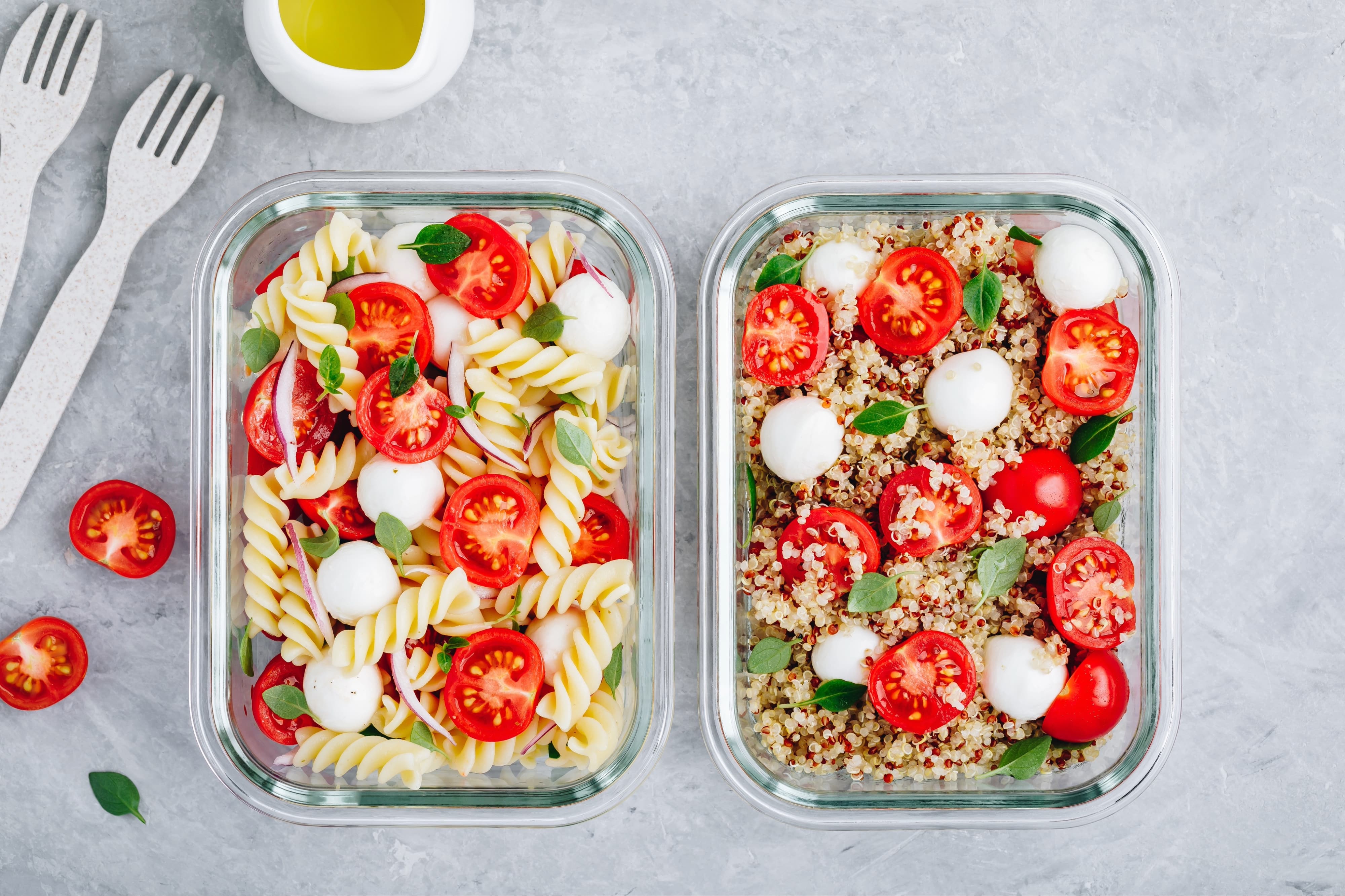 Meal prep containers with pasta salad or quinoa, tomatoes, mozzarella cheese, and basil