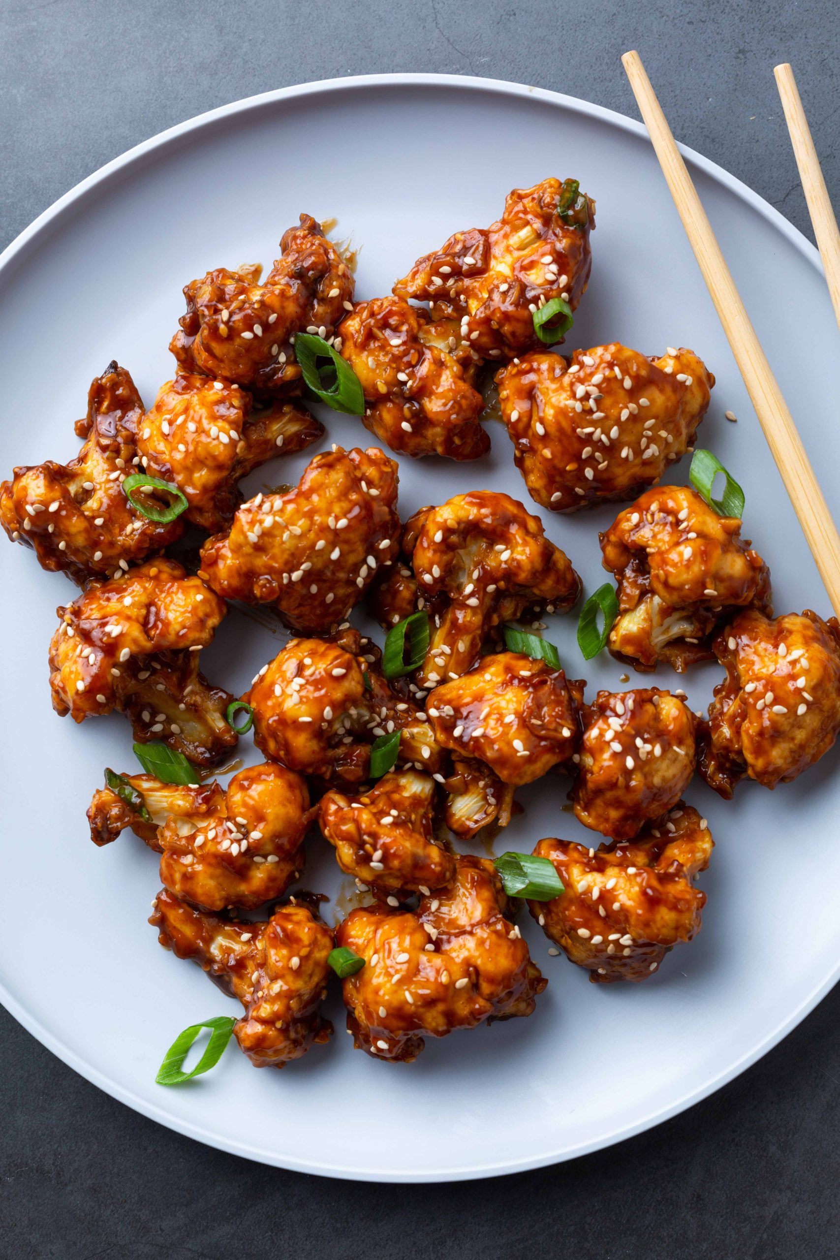 A plate of chicken wings garnished with sesame seeds and served with chopsticks