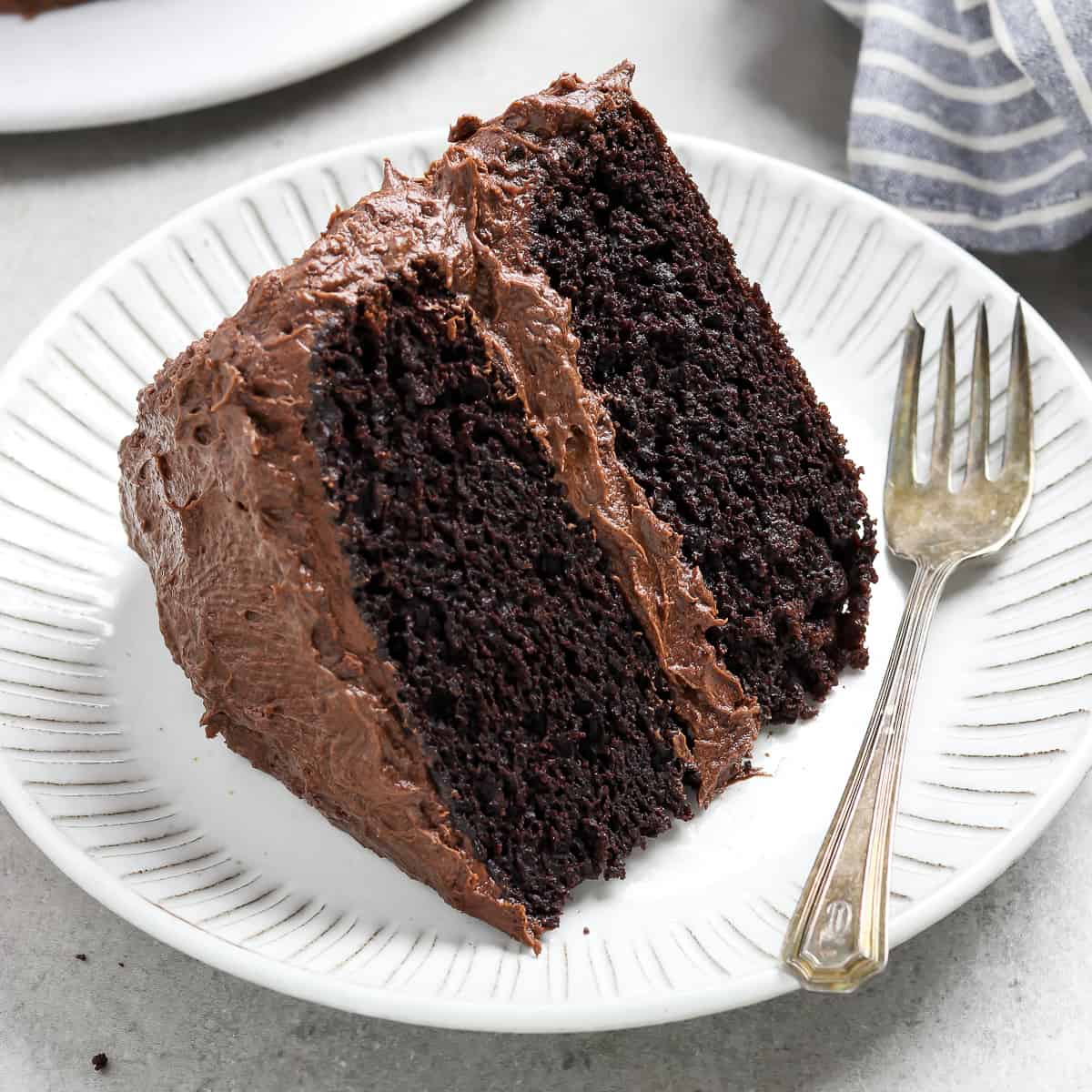 A delectable slice of chocolate cake rests on a pristine plate, accompanied by a gleaming fork