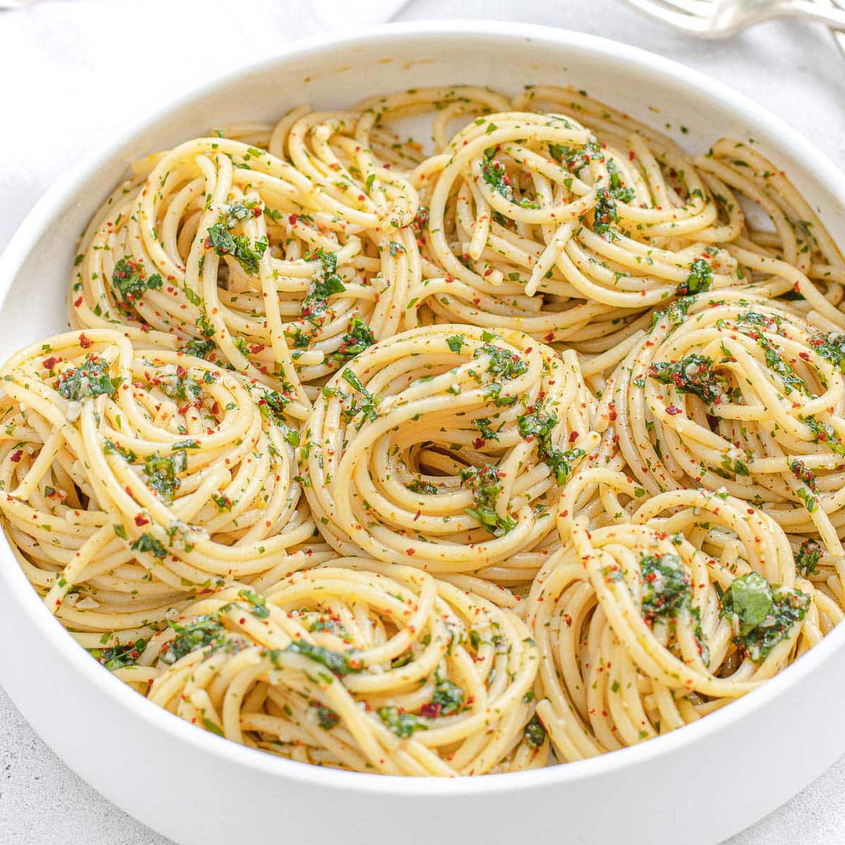 A white bowl filled with spaghetti and pesto sauce