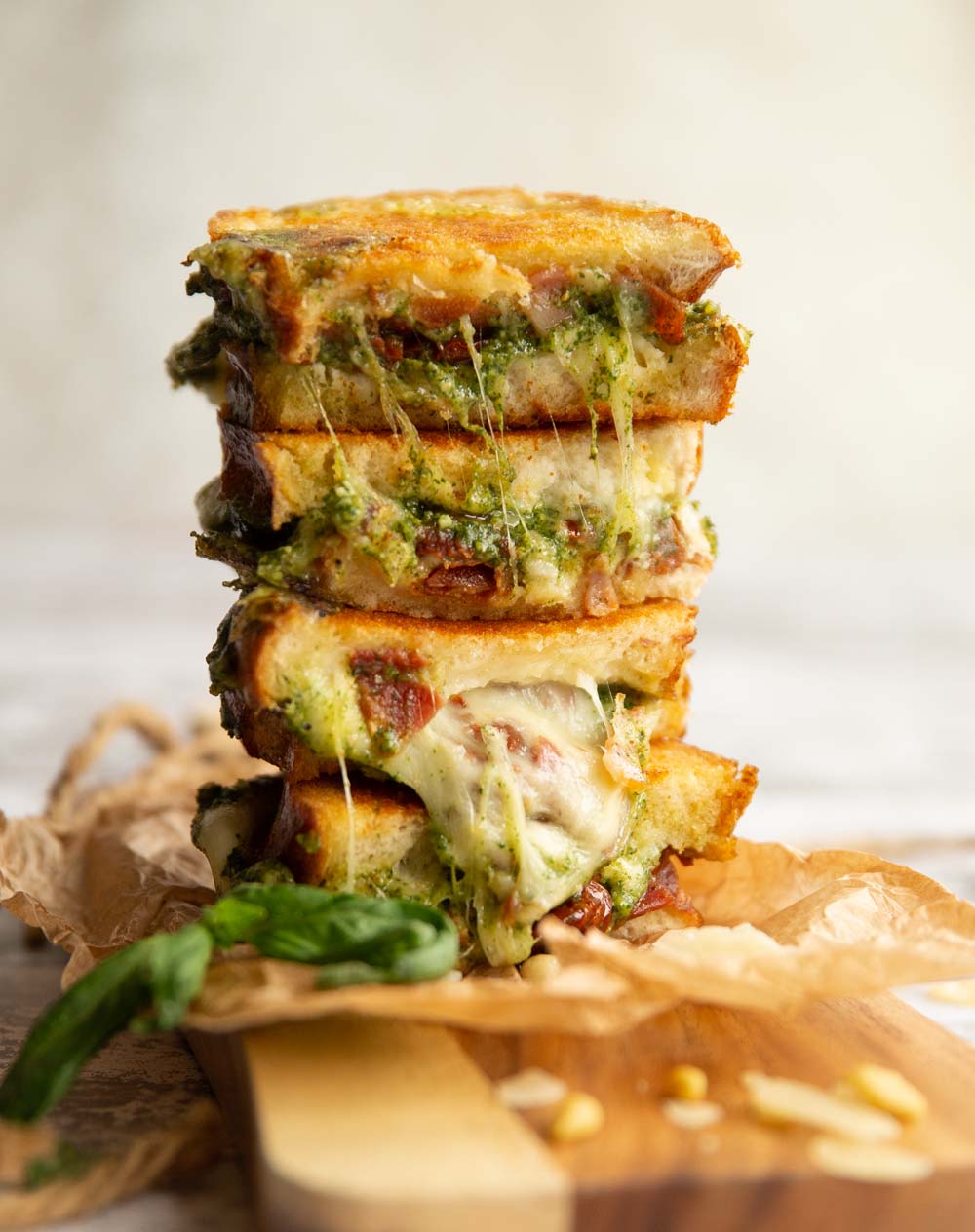 A stack of grilled cheese sandwiches topped with a generous layer of melted cheese and fresh spinach leaves