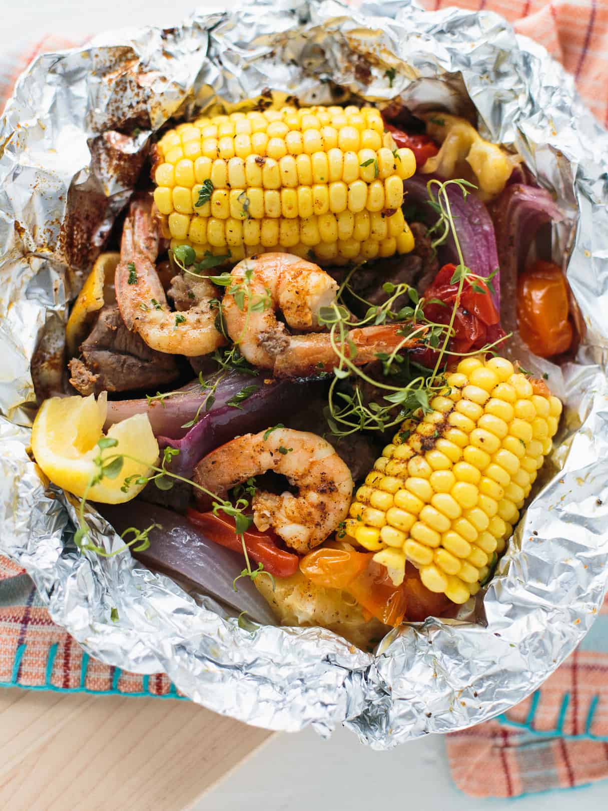 Image of delicious grilled corn, succulent shrimp, and fresh vegetables wrapped in foil