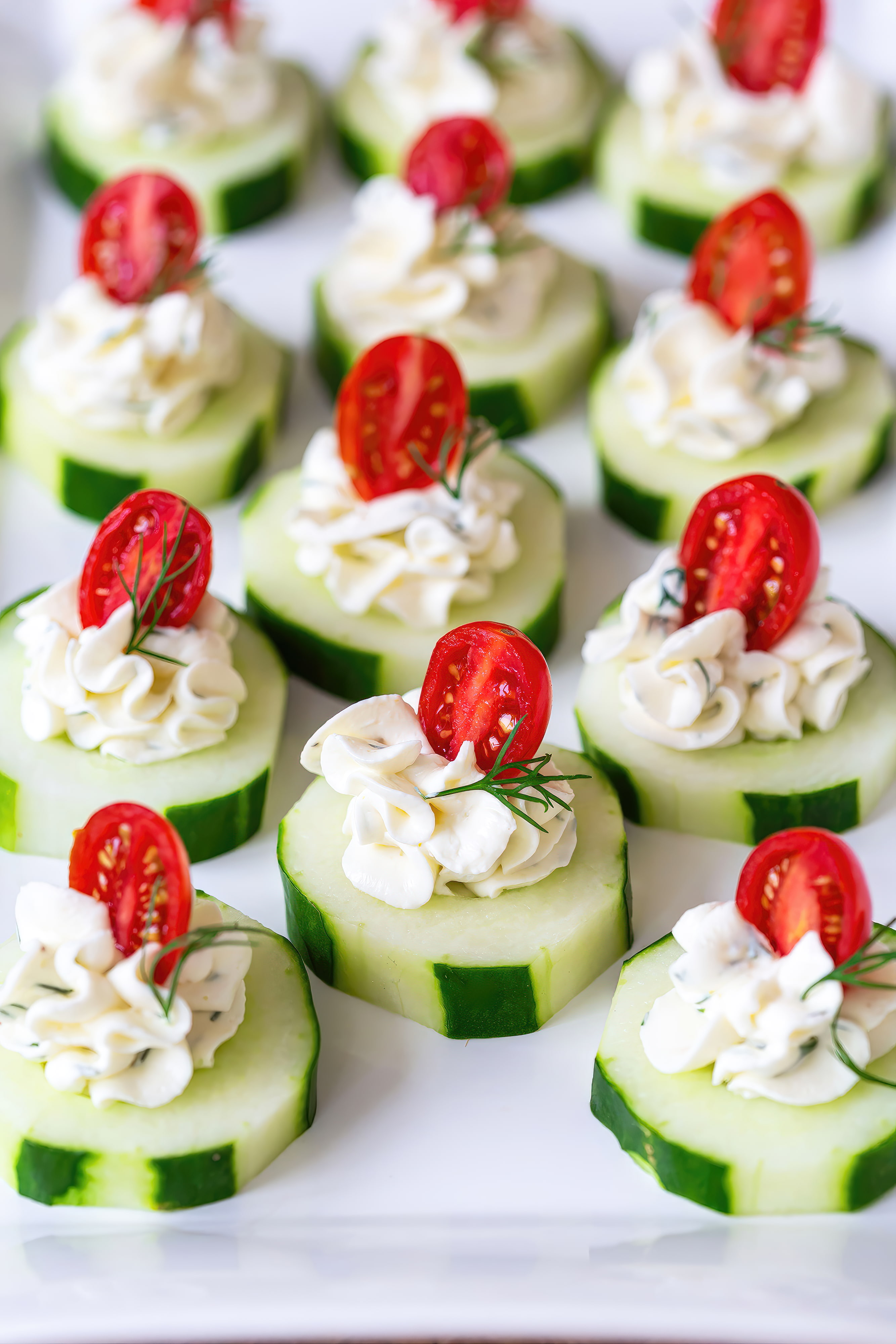 A white plate holds cucumber slices, cream cheese, and tomatoes arranged in a colorful and appetizing display