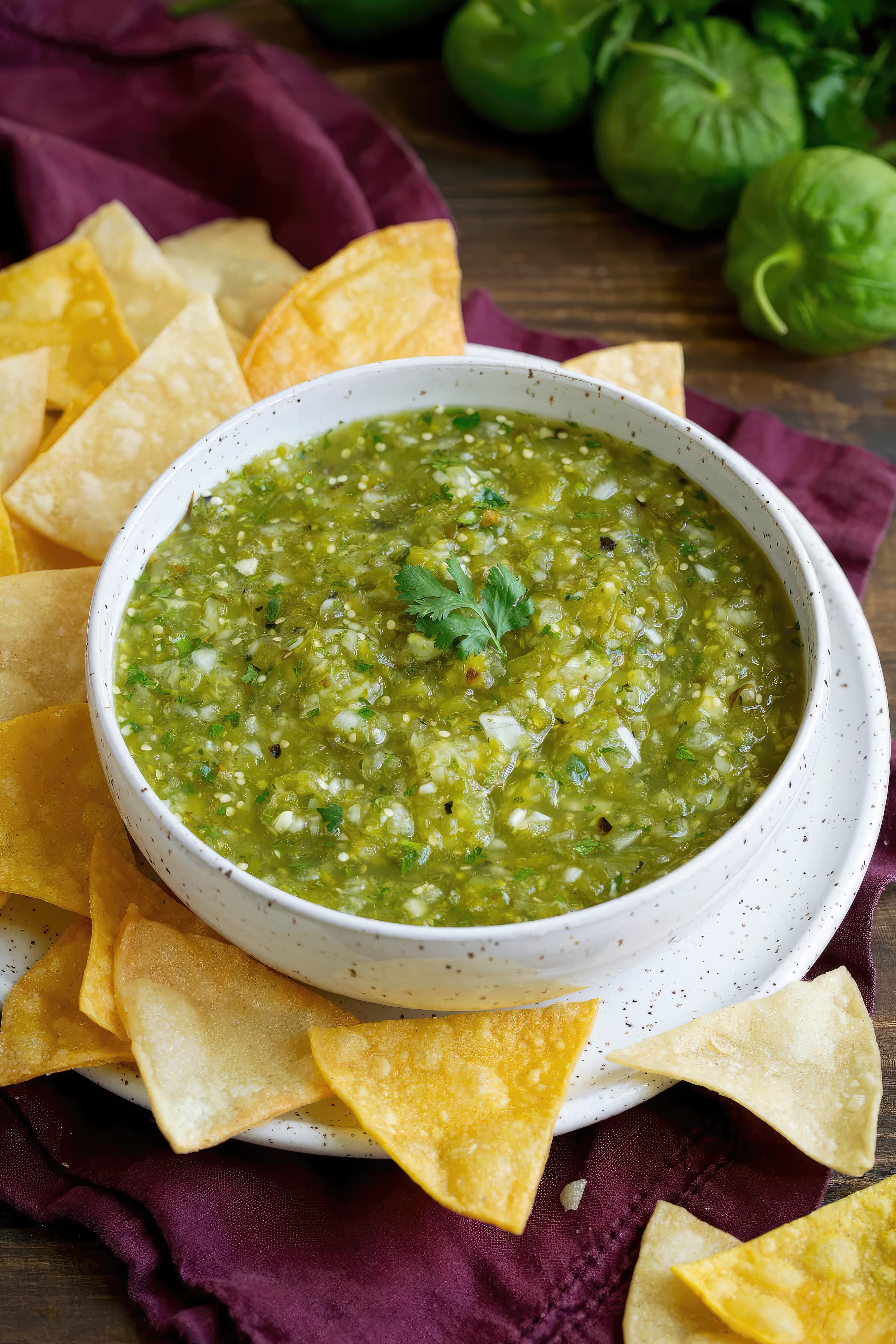 A bowl of tangy green salsa with crispy tortilla chips on the side