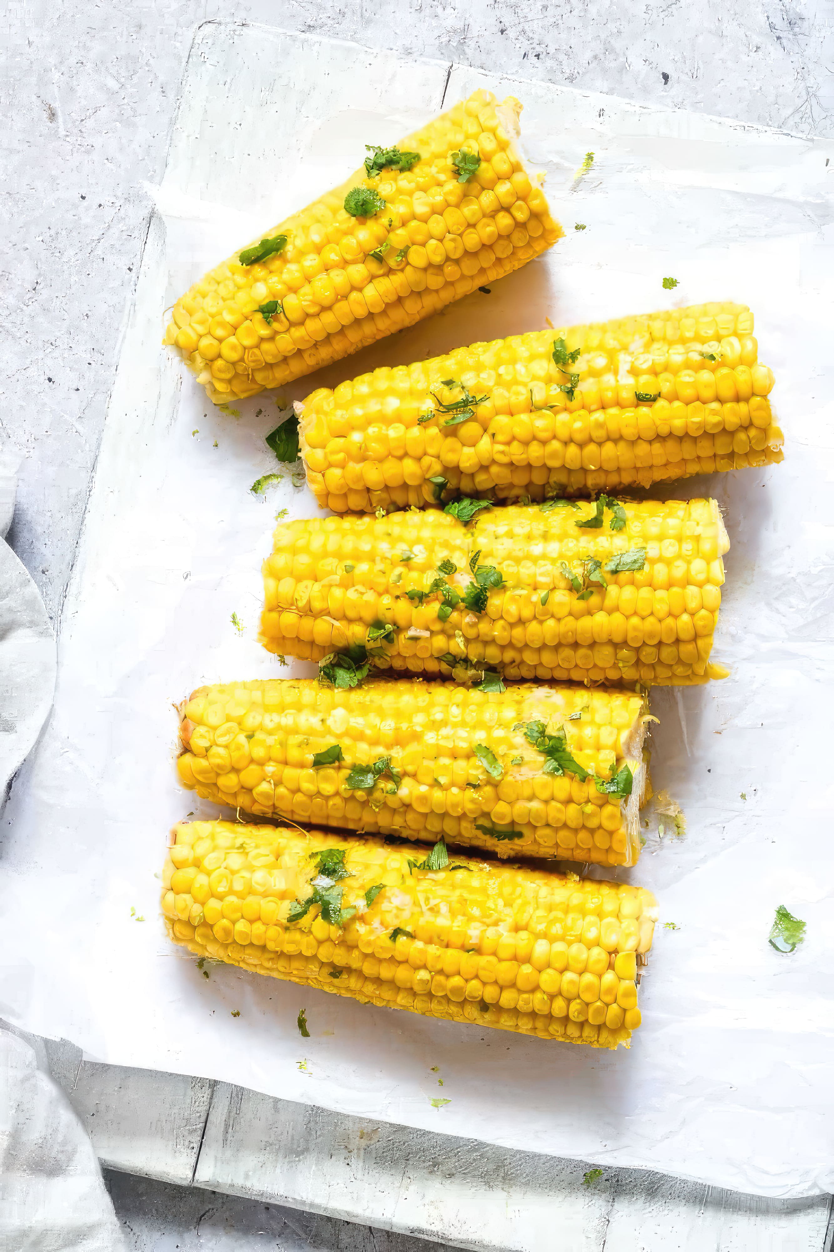 Freshly cooked corn on the cob garnished with aromatic herbs, presented on a pristine white background